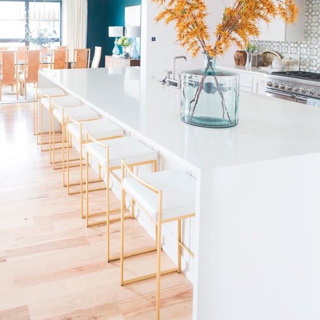 Six Heavenly Collection stools with gold stainless steel frames and white cushions lined up at a bright kitchen island.