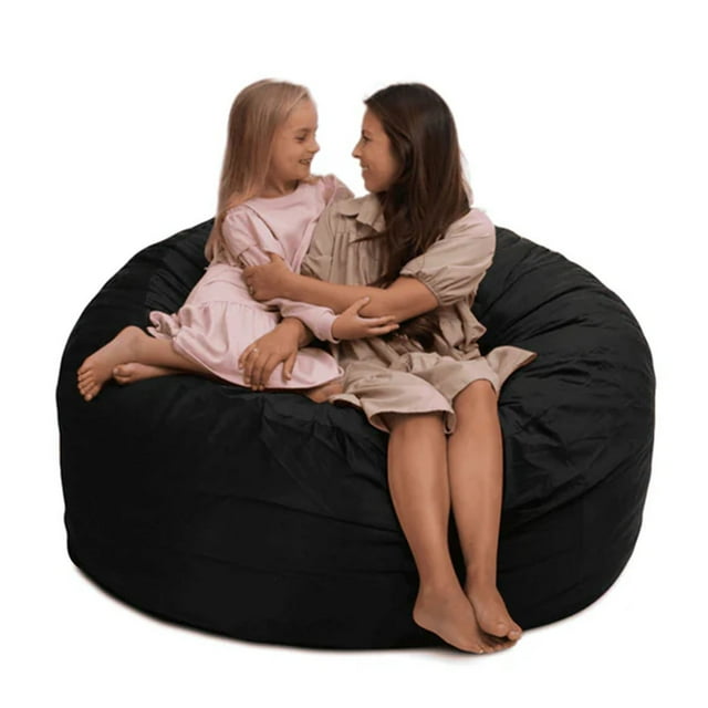 Ultimate Sack 5000 5-Foot Bean Bag Chair with a black suede cover, shown in a spacious design suitable for one to two people. The oversized foam lounger features a thick, plush suede cover with double stitching for durability and a child safety lock on the heavy-duty zipper. The chair is filled with shredded foam for balanced support and comfort, making it ideal for lounging, reading, or gaming. Two individuals are seated on the bean bag, demonstrating its roomy size and comfort.