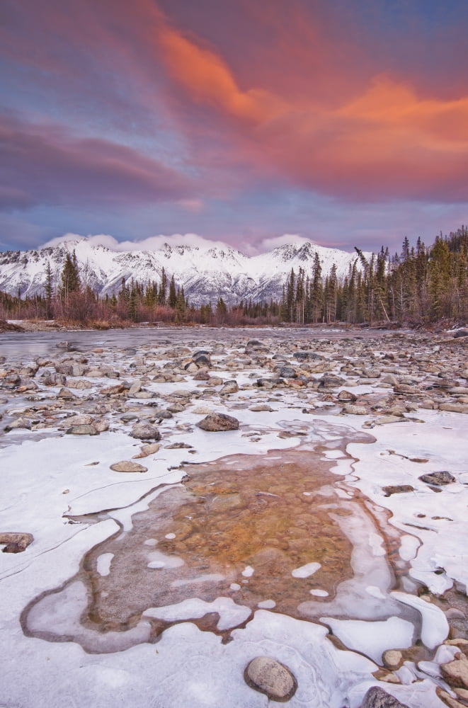 The Wheaton River In Early Winter With The Clouds Lit By Sunset Light Snow Covered Mountains Seen In The Distance Located Outside Of Whitehorse Yukon Rocks Surrounded By Ice In Foreground Canvas Art -