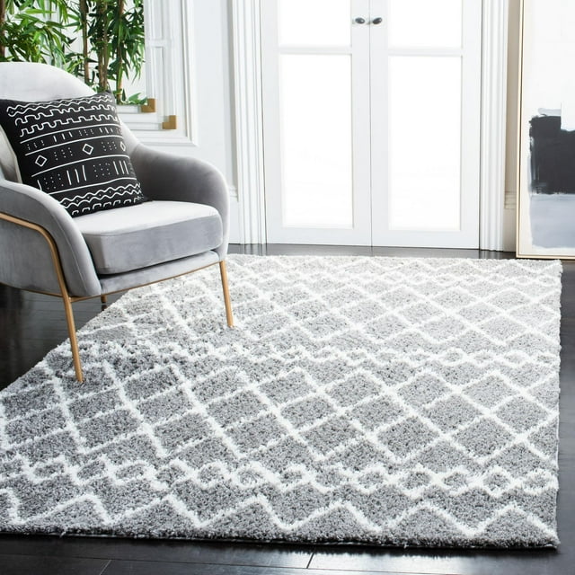 SAFAVIEH Berber Avery gray and white shag area rug featuring a geometric diamond design on dark hardwood floor next to a gray armchair with patterned black pillow.