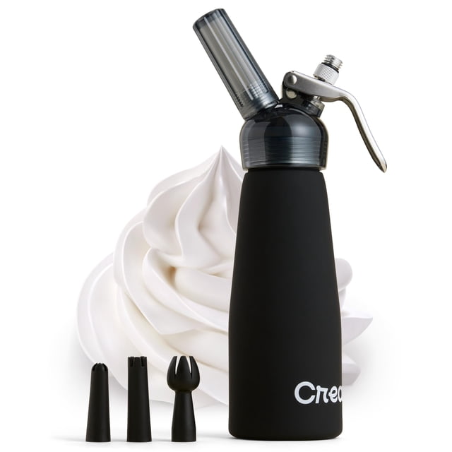 dispensador de crema batida creamright de aluminio, 500 ml, negro — Dispensador en vista frontal 3/4 con cuerpo negro mate de aluminio, cabezal compuesto transparente y palanca metálica, acompañado de tres boquillas negras y una porción de crema batida blanca; ideal para decorar postres, rellenar bollería y preparar bebidas con espuma casera, y a menudo usado también para dosificar cremas y coberturas en repostería doméstica.