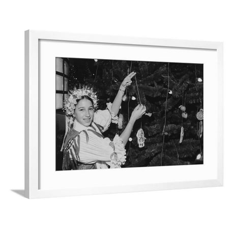 A Girl Decorating One of the Many Ethnic Themed Trees During the Annual Christmas around the World Framed Print Wall (Best Christmas Tree Decorating Themes)