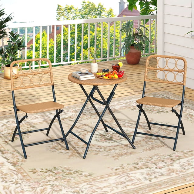 Costway 3 PCS Patio Bistro Set with Wicker Seat & Tabletop, including two folding light brown PE rattan chairs and a matching round table with a sturdy black metal frame. Ideal for outdoor small spaces like balconies, backyards, or gardens, the set is shown on a wooden deck with a decorative rug and surrounded by greenery and potted plants.