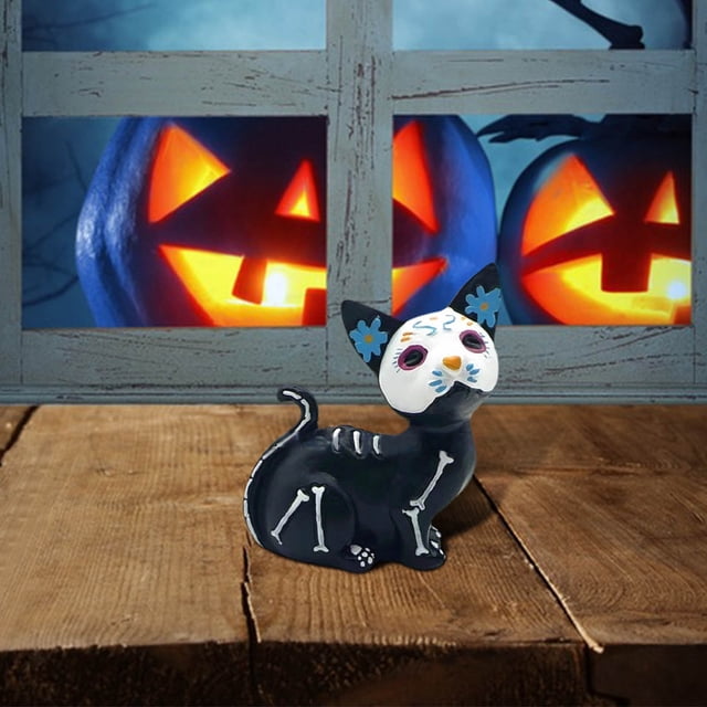 estatua de perro día de los muertos figura de resina | adorno de perro esqueleto de halloween — figura multicolor vista 3/4, perro sentado de resina con cuerpo negro y huesos pintados en blanco y cabeza blanca decorada con flores y motivos azules y rosas; apoyado sobre mesa de madera frente a ventana con calabazas iluminadas, pensado como adorno para mesa, escritorio o estantería en decoraciones de Halloween y Día de los Muertos; a menudo usado también en proyectos de manualidades.