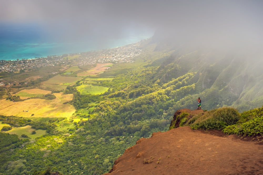 A man standing on the edge of a cliff on the Kuliouou Ridge Trial enjoys the view of Oahus windward side and the town of Waimanalo as the clouds roll in on a summers day Waimanalo Oahu Hawaii United S