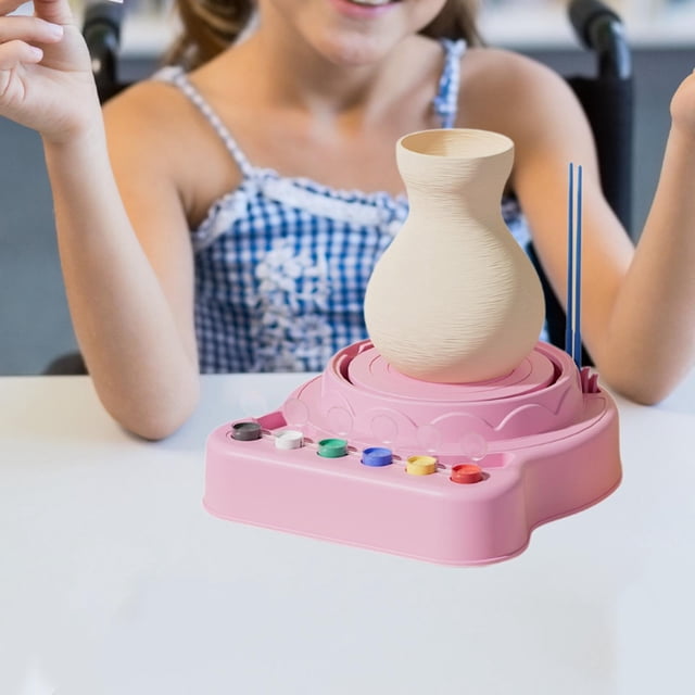 vuela de cerámica para niños kids art and craft diy creative educational toy toy clay sculpting actividad para la clase de cerámica niños de bricolaje rosa máquina de cerámica eléctrica rosa, vista frontal centrada con vasija de arcilla cruda en la rueda, tablero frontal con seis pinturas pequeñas, dos palillos y controles de velocidad visibles; fabricada en PP, tamaño 20CMX25CMX23CM (7.87x9.84x9.06 in), alimentada por cable USB incluido y diseñada para modelado, coloreado y secado al aire. Suele usarse también para prácticas de manualidades en clase.