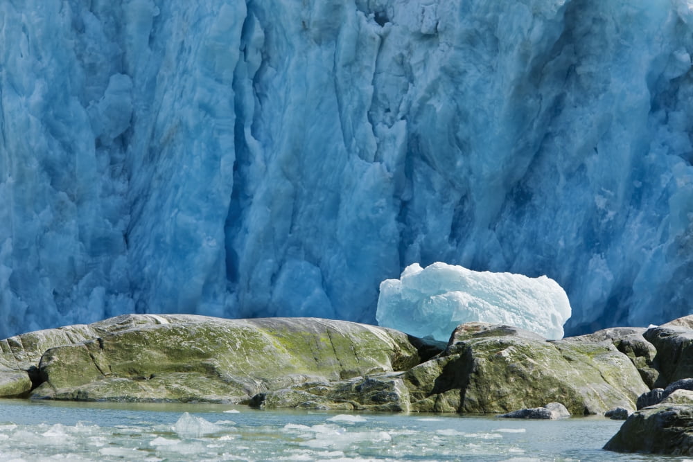 An Iceberg Rests On The Top Of Boulders After Being Tossed On Shore By The Tidal Wave From Calving Dawes Glacier In The Background Endicott Arm Southeast Alaska Summer Canvas Art - Ray Bulson Design