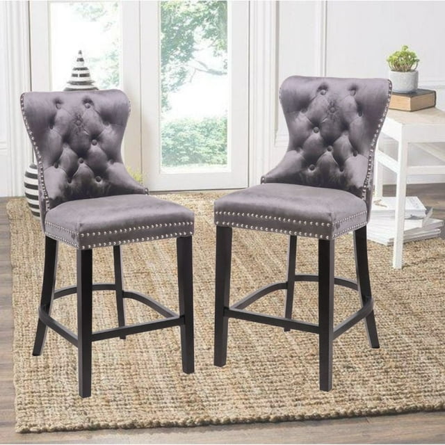 Set of two vintage-style Ley counter stools upholstered in black velvet with button-tufted backs and silver nailhead trim, featuring dark wooden legs, placed on a natural fiber rug near large windows.