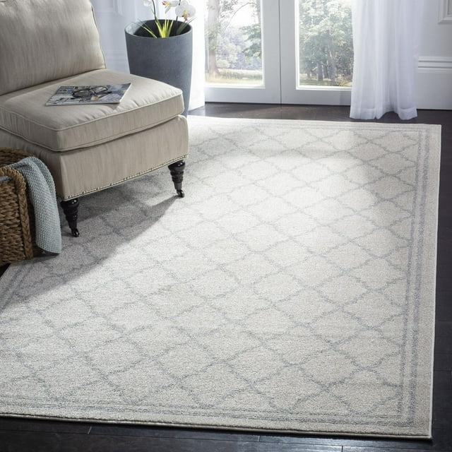 SAFAVIEH Amherst Trina light gray geometric area rug in a bright room with dark wood floor and beige armchair.