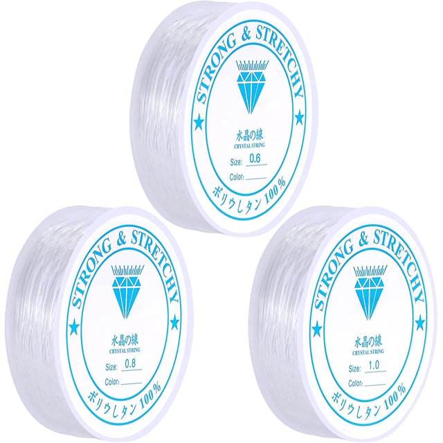 hilo elástico brillar transparente para pulsera juego de 3 cordones elásticos para cuentas de cristal 0,6 mm 0,8 mm 1,0 mm — tres rollos en vista frontal 3/4 con hilo transparente enrollado en carretes blancos y etiquetas azules que muestran el tamaño; brillo translúcido del hilo TPU visible y borde de carrete liso sobre fondo blanco. Suele usarse también para colgar adornos y proyectos de manualidades familiares.