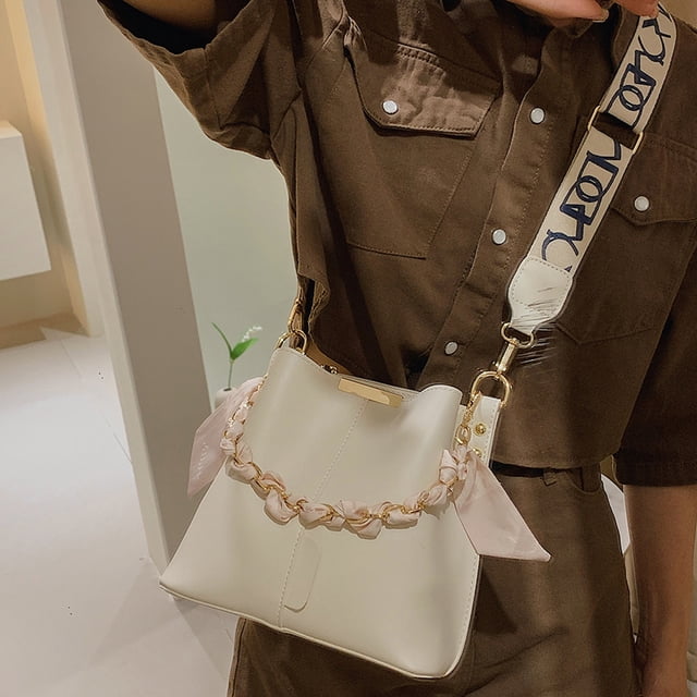 bolso de hombro con cadena de lujo bolso de mano de diseñador de cuero pu con correa ancha para mujer blanco, vista 3/4 frontal de bolso tipo cubo (8.66 x 8.27 x 4.33 pulg.), PU blanco con cierre de cerrojo, cadena decorativa entrelazada con lazo rosa y correa ancha con letras, llevado al hombro en ambiente interior.