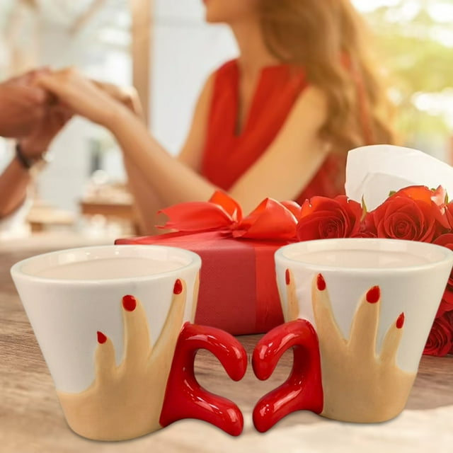 fiudx juego de tazas para pareja en cerámica, set de 2 tazas blancas con detalle de manos doradas y asas rojas que forman un corazón al juntarlas; mostradas sobre mesa junto a caja de regalo roja y rosas, ideal para café y agua, 25 x 18 x 15 cm; también aptas para servir infusiones pequeñas.