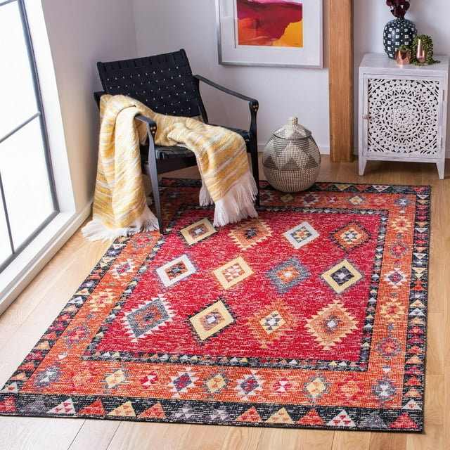 SAFAVIEH Montage Faris Southwestern outdoor area rug featuring vibrant red and orange geometric designs placed on wood flooring beside a modern black woven chair with yellow throw.