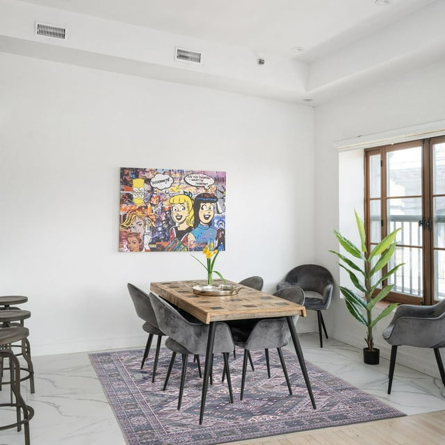 ECARPET vintage Turkish flatweave area rug featuring muted purple and pink geometric designs, placed under a wooden dining table surrounded by six gray velvet chairs in a bright, modern indoor space.