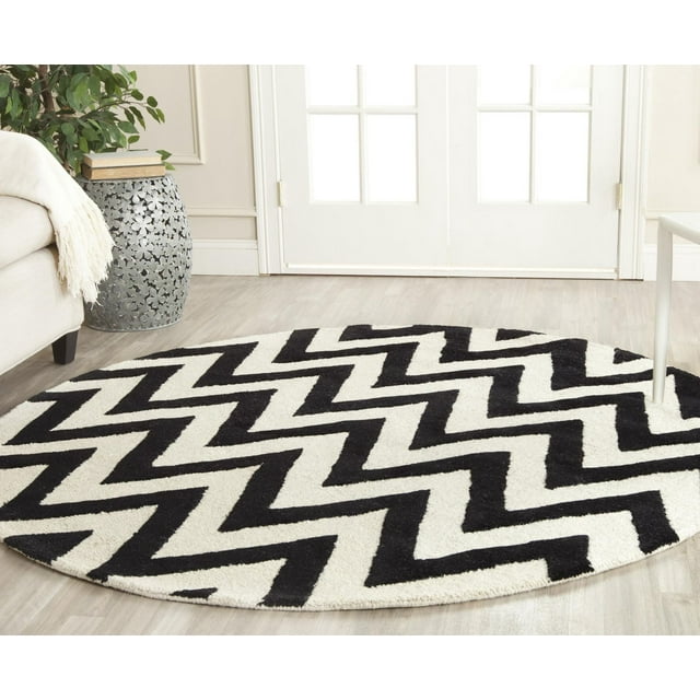 Round Safavieh Cambridge Kaitlyn area rug featuring bold black and white zig zag stripes, placed on light wood flooring in a modern living space.