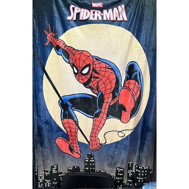 exclusiva! cobija frazada ultra suave spider-man telaraña. Cobija vista frontal con gran ilustración de Spider-Man en pose dinámica, traje rojo y azul con patrón de telaraña, círculo amarillo tipo luna detrás y silueta de edificios negros en la base; logo Marvel y texto SPIDER-MAN en la parte superior. Tejido de felpa visible; también suele usarse como manta decorativa para sillón o para llevar en viajes cortos.