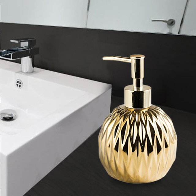 dispensador de jabón de cerámica perfecl lujo estilo a — dispensador cerámico con cuerpo esférico facetado y acabado dorado, 8.4 cm x 11.5 cm; cabezal con bomba manual metálica para jabón líquido, loción o champú, colocado sobre encimera de lavabo en baño moderno; también usado como dispensador de tocador para cremas.