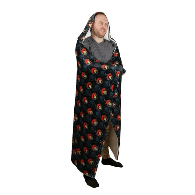 NHL Ottawa Senators Hooded Blanket, 50" x 70", worn by a standing person, featuring a black exterior with repeated Ottawa Senators logos in red and beige, sherpa-lined hood and interior, designed for warmth and comfort during indoor or outdoor use, also suitable for cozying up on summer nights by the fire.