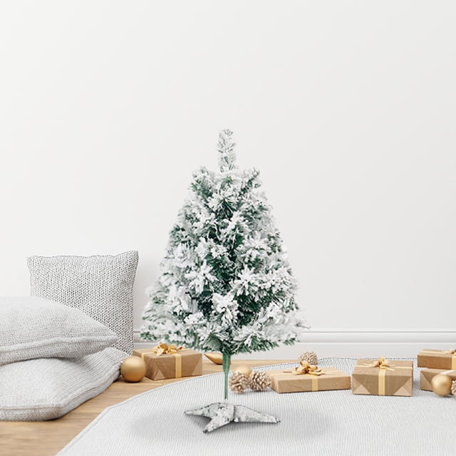 fiudx árbol de navidad con nieve, 45 cm, ramas ajustables y base metálica estable. Vista frontal centrada de un árbol verde con nieve artificial en las ramas y silueta cónica compacta; montaje sencillo con la base de estrella metálica visible. Colocado en interior sobre alfombra junto a cojines y regalos, también apto como adorno de mesa.
