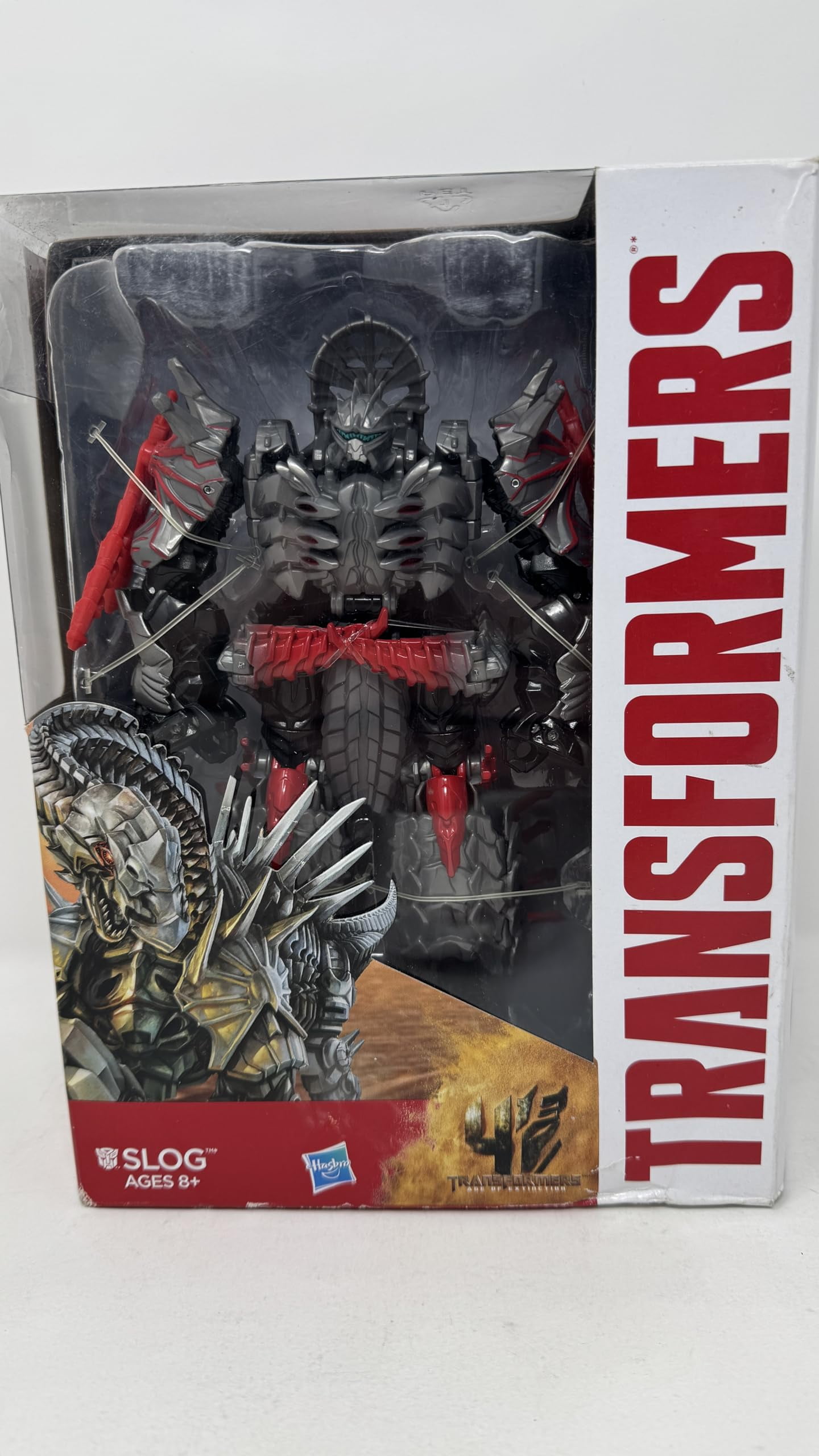 Transformers Age Of Extinction – Figura Slog Voyager Class, 2 In 1, Si Trasforma Da Robot A Dinosauro, Con 2 Spade