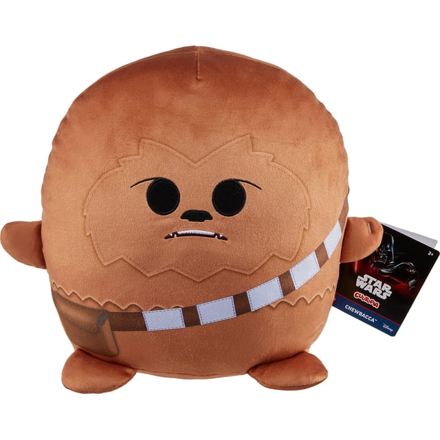 peluche chewbacca cuutopia star wars 25 cm mattel muñeca almohada redondeada color marrón con cara bordada y ojos negros, bandolera estampada tipo cartucho cruzando el torso, brazos y patas cortos, peluche coleccionable con etiqueta visible, vista frontal centrada sobre fondo blanco. Suele usarse también como almohada para siestas o decoración de habitación.