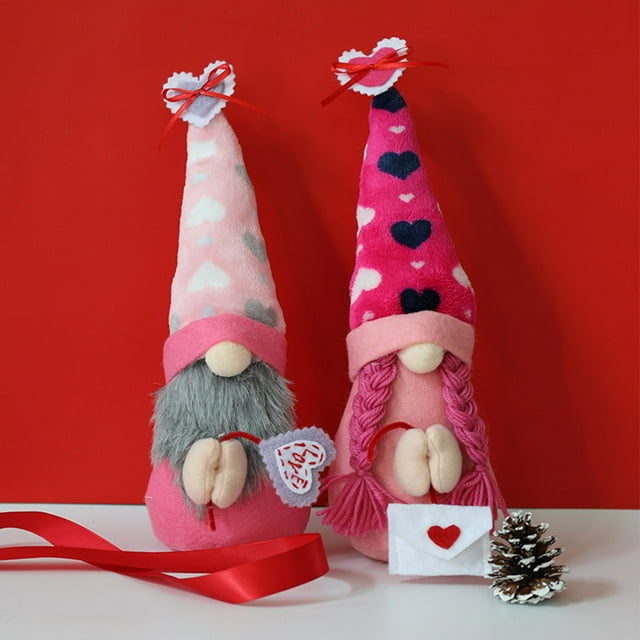 fiudx gnomo de san valentín muñeco sin rostro con sombrero de amor, 1 juego de M: vista frontal de dos gnomos de tela rosa con gorros altos estampados de corazones, uno con barba gris y otro con trenzas rosas, narices redondas y manos sosteniendo un corazón y una bolsita, sobre fondo rojo con cinta decorativa.