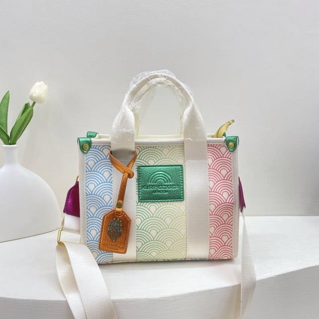 kurt geiger-bolso de mano de lona para mujer, bolsa de hombro de gran capacidad, de marca de diseñador de lujo, tendencia de moda, novedad de 2024 Bolso tote blanco de lona, vista frontal centrada con asas cortas y correa bandolera blanca ajustable. Paneles a rayas en azul, verde, amarillo y rosa, placa de marca verde en el frente, etiqueta colgante marrón y herrajes dorados; especificado con cremallera e interior con bolsillo ranurado y bolsillo para móvil. A menudo usado como bolso diario para trabajo ligero o salidas casuales.