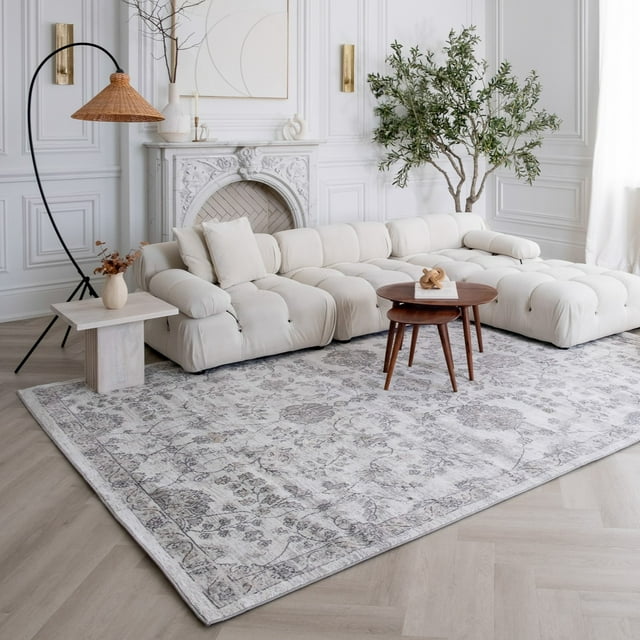 Beige grey floral Rug Branch Atlas Classic indoor area rug displayed under a white tufted sectional sofa with wooden coffee tables in an elegant living room setting.