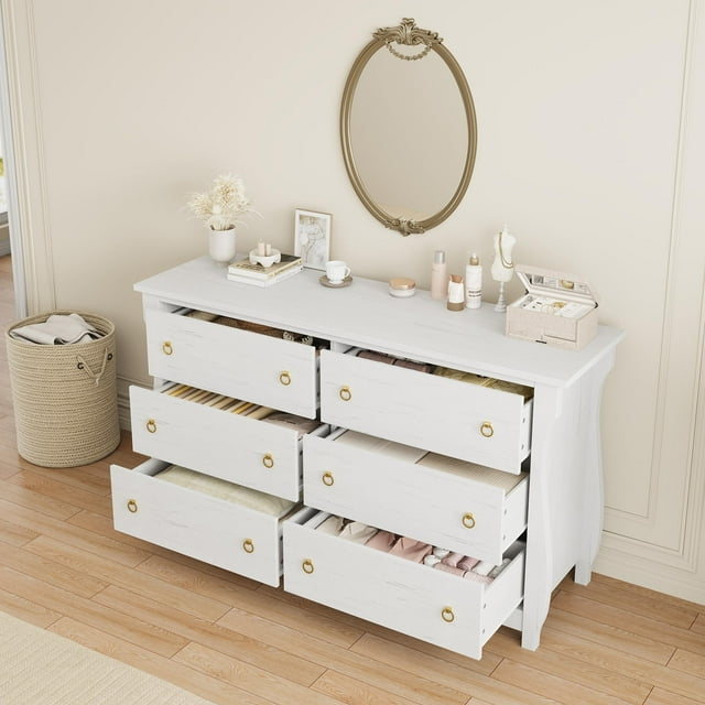 AKDSteel Commode 6 pour Chambre, Coffre de Rangement en Bois de 47,2 Pouces de Large avec six Tiroirs Profonds, Présenté dans une Pièce de Couleur Claire. la Commode Présente un design d'Inspiration Bohème avec des accents en Rotin Faits à la Main, des Pieds Courbés et des Poignées Anneau Ton or. la surface Supérieure Spacieuse Est Stylée avec des Articles de Déco, Y Compris un Miroir, une Boîte à Bijoux et des Cosmétiques. les Tiroirs Sont Partiellement Ouverts, Révélant des Vêtements et du Linge Bien Organisés. Fabriquée en Bois d'Ingénierie en MDF durable, Cette Commode Autoportante
