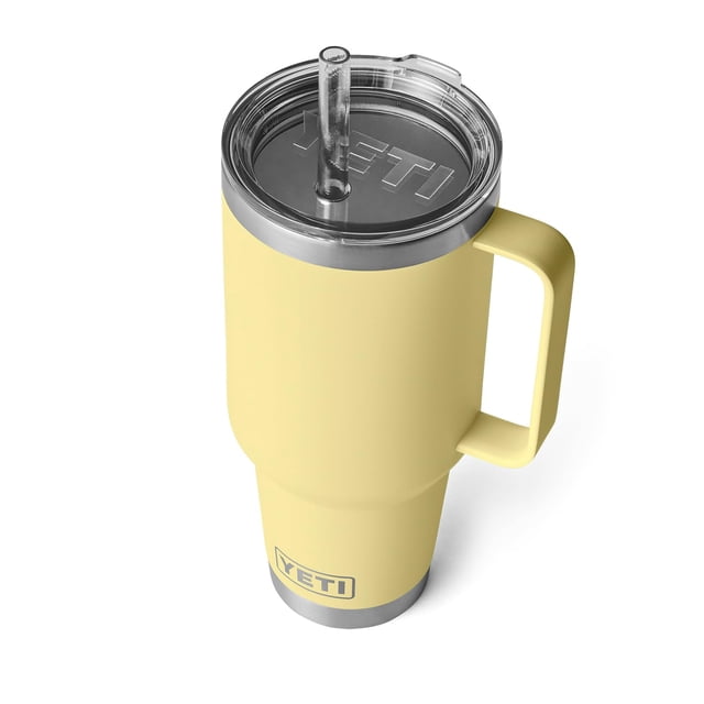 Taza YETI Rambler de 1,25 L con pajita, vista en 3/4 desde arriba de una taza amarilla con mango elevado, tapa transparente con popote cristal y logo YETI; cuerpo de acero inoxidable 18/8 con aislamiento al vacío de doble pared, diseño sin sudor y base compatible con portavasos, ideal para llevar bebidas frías en viajes.
