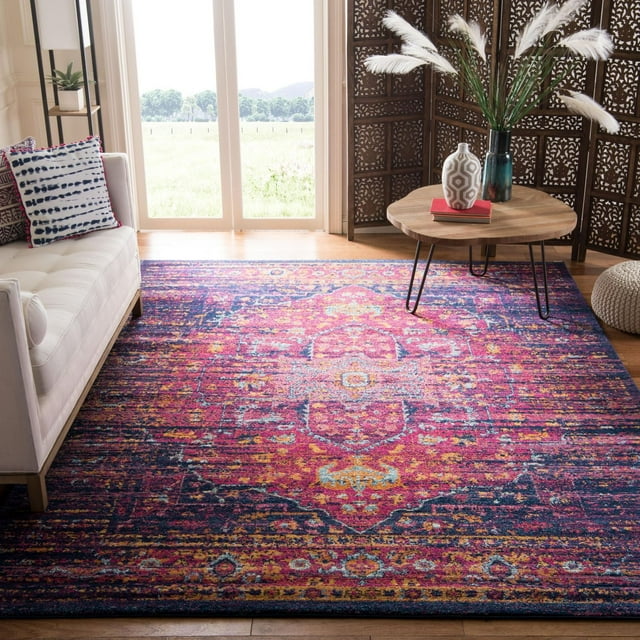 Safavieh Evoke Westley Traditional Area Rug featuring a vibrant multicolor frieze pattern in pink, blue, and yellow, power-loomed from durable polypropylene yarns. Positioned on a hardwood floor beneath a round wooden coffee table with metal legs, styled with decorative vases and pampas grass, next to a white sofa with patterned cushions and a carved wooden room divider, suitable for adding durable, stylish accent to living rooms.