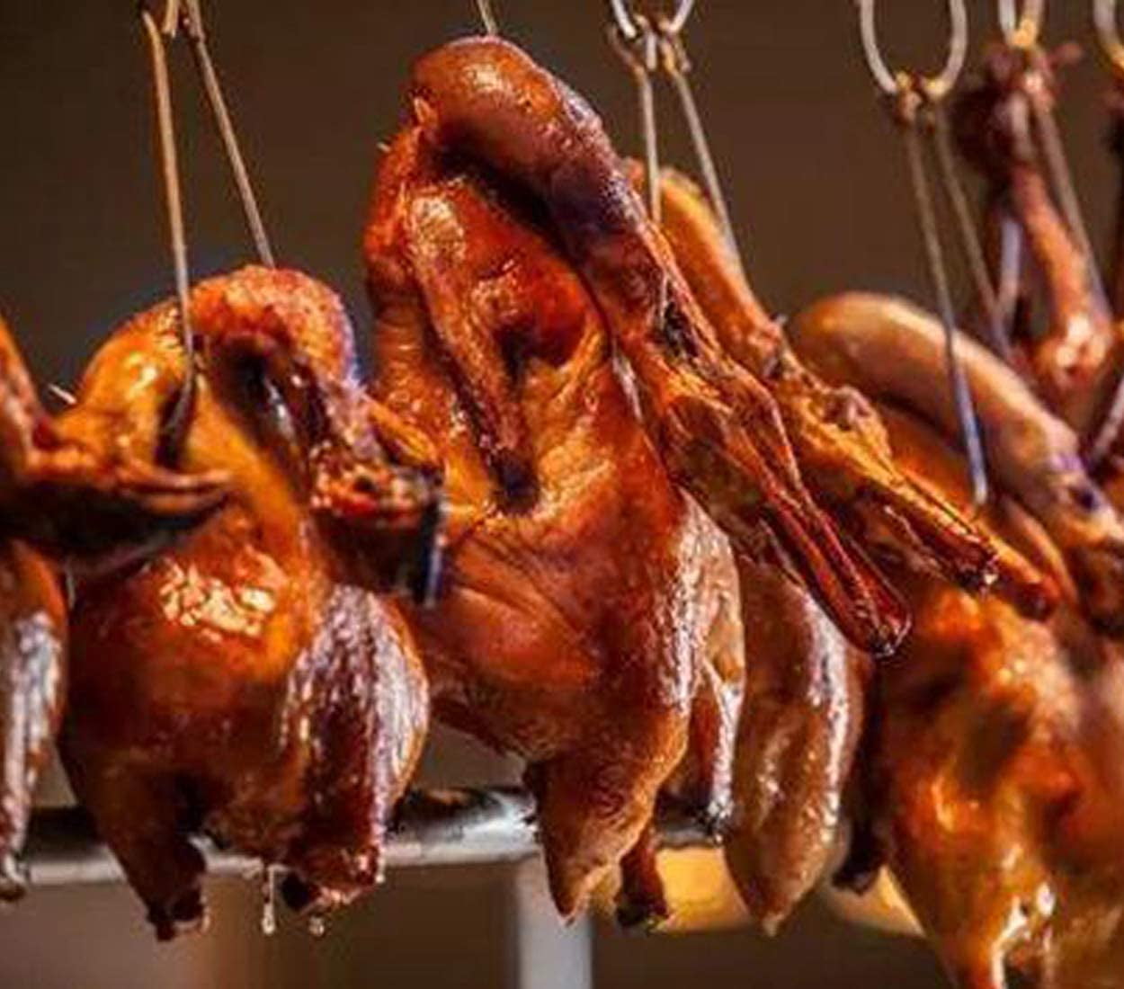 Roasted ducks hanging from metal meat hooks in the window of a