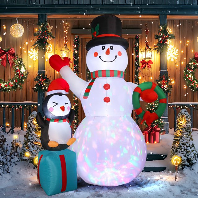 regalo inflable navideño con muñeco de nieve, 2,1 m, con luces led — Muñeco de nieve inflable de 2.1 m con sombrero de copa negro y bufanda a rayas, acompañado de una caja de regalo con pingüino inflable y corona; vista frontal nocturna con luces LED integradas en el torso esférico, porche decorado con guirnaldas; incluye soplador, cuerdas y estacas para anclar. Ideal para decorar césped y jardín.