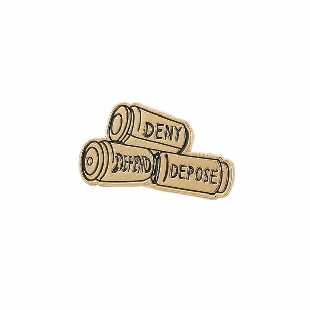 Broche con forma de bala en tono dorado con la inscripción «Deny Defend Depose»