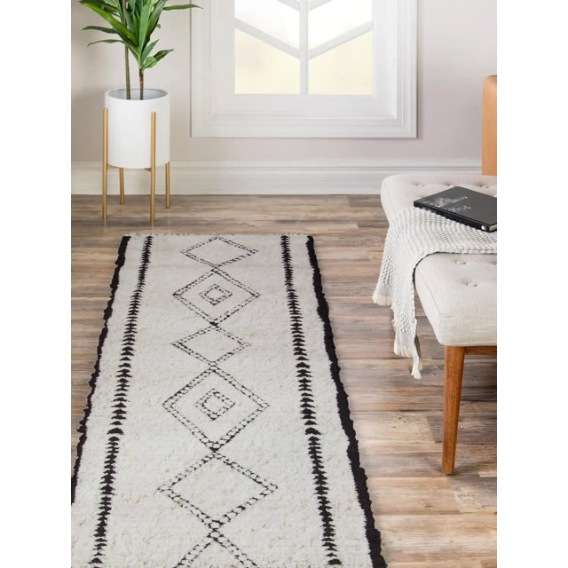 ECARPET Zelda contemporary runner rug featuring black geometric diamond patterns on a white background, placed on wooden floor in a bright living room with potted plant and beige bench