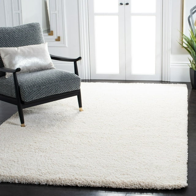 Safavieh Milan Harlow solid white shag area rug displayed in a modern living space beneath a black-framed armchair with patterned upholstery.