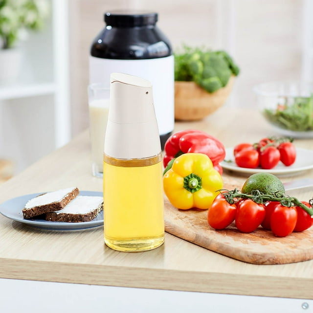 xihbxyly aceitera botella de vidrio de apertura automática color amarillo, vista frontal centrada de botella cilíndrica con tapa dispensadora automática blanca y vidrio transparente que muestra aceite claro y tanque grueso, sobre mesa de cocina junto a tabla con tomates cherry y pimiento en ambiente de preparación; a menudo se usa como dispensador de aceite, vinagre o salsa para cocinar.