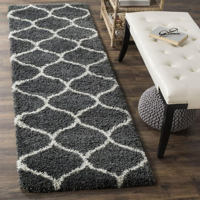 Gray Safavieh Hudson Arline shag area rug featuring a white geometric trellis pattern, styled in a room with wooden flooring, a tufted bench, and wicker shelving.