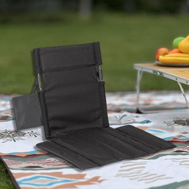 asiento de estadio con cojín para gradas, portátil, con bolsa de transporte, silla plegable para gradas. negro asiento plegable negro con respaldo alto (39 x 40 cm) y cojín de asiento amplio (33 x 54 cm); paneles acolchados en tela Oxford, bolsillo lateral de almacenamiento y postes de aleación de aluminio visibles. Vista en 3/4 sobre una manta en exteriores; adecuado para estadios, camping o picnics como soporte ergonómico portátil.