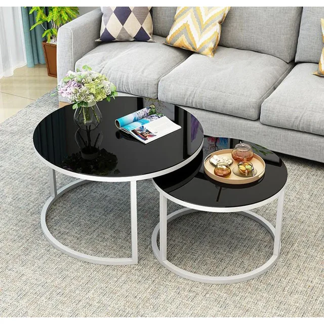 mesa de centro redonda de vidrio templado para sala de estar 2 en 1, juego anidado con tablero de vidrio templado negro y base de hierro blanco; grande 70×70×45 cm y pequeña 50×50×38 cm; vista frontal junto a sofá en sala moderna estilo Europa y América; montaje sencillo; ideal para revistas y accesorios decorativos.