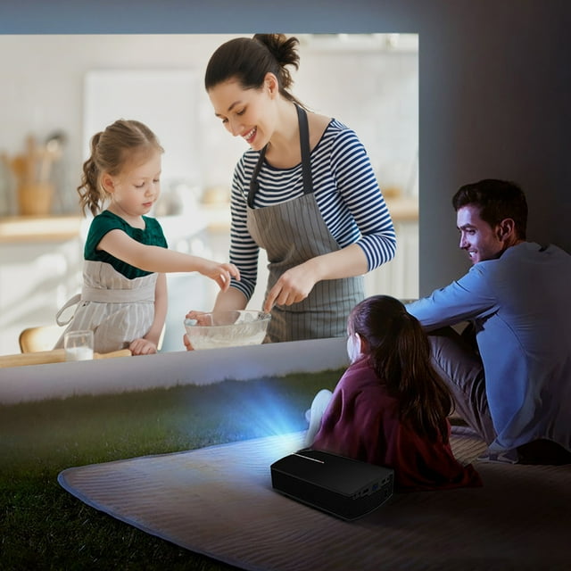 proyector led portátil de alta definición para oficina y hogar, pantalla grande de 130 pulgadas, corrección trapezoidal, reflexión difusa, protección ocular, miniproyector negro FcBaudy — Vista 3/4 frontal de un miniproyector compacto sobre una manta proyectando una escena familiar grande; carcasa negra con haz de luz azul y puerto lateral visible, proyección ajustable 50–130 in y corrección trapezoidal ±15° manual; apropiado para cine en casa y uso al aire libre, a menudo usado también para presentaciones móviles.