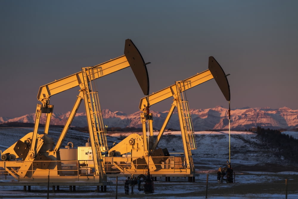 Two pump jacks at sunrise reflecting the warm morning light in a snow covered field and snow covered foothills and mountains in the background lit by the morning sun Alberta Canada Canvas Art - Michae