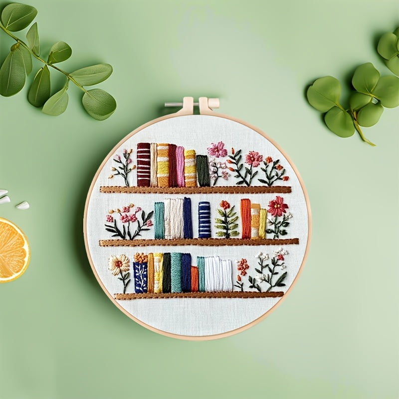 An Embroidery Kit Featuring a Bookshelf Floral Pattern Measuring, Suitable for Both Adults And Beginners. It Includes Instructions, Printed Fabric, an Embroidery Hoop, And Needle And Thread