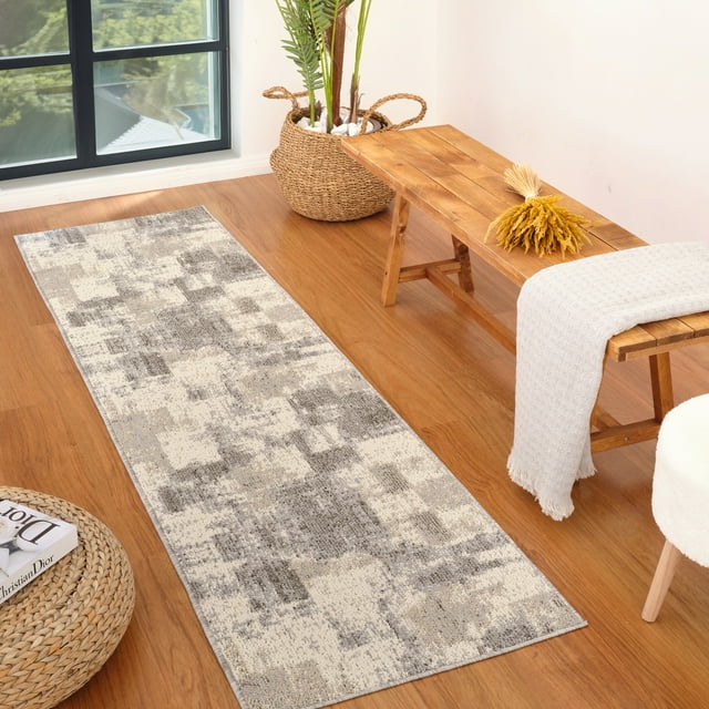 Modern abstract grey and beige indoor area rug placed on wooden floor next to a wooden bench with white throw in bright living space.