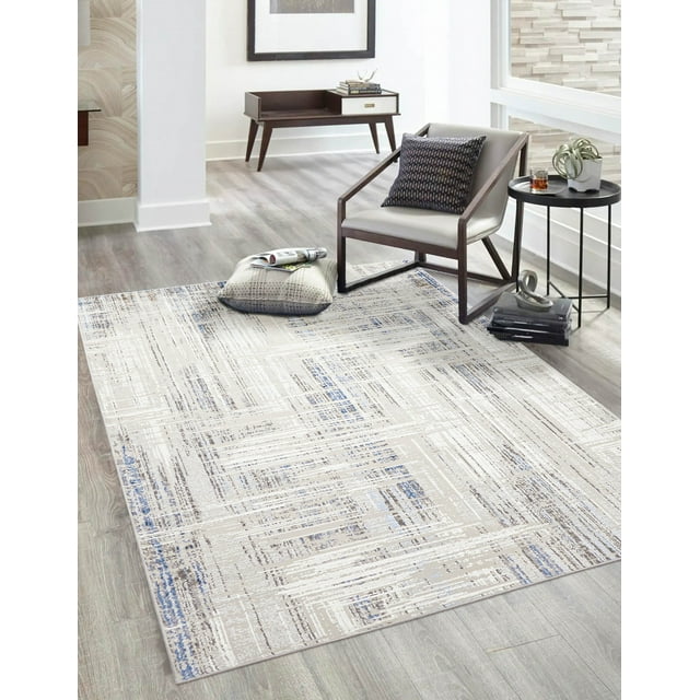 ECARPET Efes Contemporary/Modern Area Rug for Living Room, Bedroom, Dining Room, Entrance, Hallway and More displayed in a bright room with light wood flooring. The rug features a neutral beige base with abstract distressed linear patterns in white, brown, and soft blue. It is paired with a modern wooden armchair with grey upholstery and a patterned pillow, a black round side table holding a plant and glass, and a wooden console table in the background. This low-maintenance rug is suitable for various rooms and ideal for creating a calm, contemporary space.