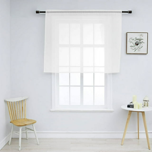 1Pc Solid Color Modern Sheer Small Curtain for Kitchen and Living Room, measuring 52 x 36 inches, displayed in a bright room. The curtain is semi-transparent, filtering sunlight while maintaining privacy. It is hung on a black curtain rod over a window with a white frame. The room features minimal decor, including a wooden chair and a small round table with candles and books.