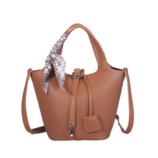 bolso de diseño de nicho de alta gama para mujer 2025, pequeño bolso de cubo portátil marrón en PU granulada, vista frontal con cierre de cremallera superior y cordón decorativo con colgante; asa corta y correa larga ajustable, forro de poliéster y compartimento interno tipo sándwich con cremallera, estilo simplicidad urbana para uso diario; suele usarse también para organizar artículos personales en viajes cortos.