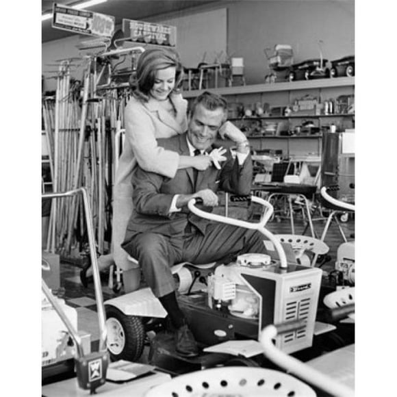 Posterazzi SAL25543705 Mid Adult Man Sitting on a Lawn Mower with a Mid Adult Woman Standing Behind Him in a Store Poster Print - 18 x 24 in.
