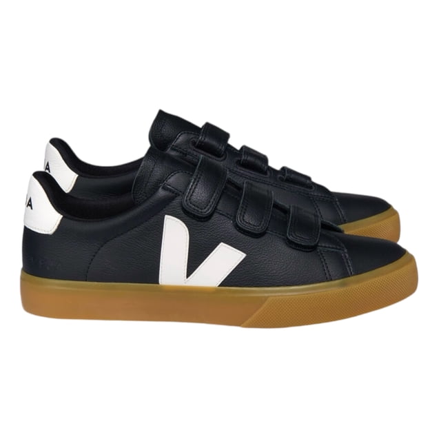 tenis veja chrome negros con logo blanco y cierre de broche vista 3/4; par de tenis negros con superficie tipo piel, suela de goma color caramelo, gran 'V' blanca en el costado, talón blanco con VEJA en negro y tres cierres de broche en la parte superior sobre fondo neutro. A menudo usados como opción cómoda para uso urbano diario.