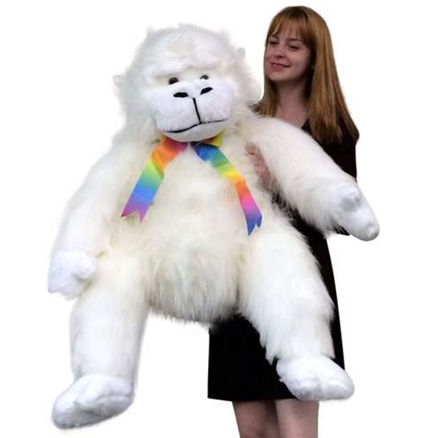 American Made Giant Stuffed White Gorilla Monkey, a 40-inch soft and fluffy plush animal with long white fur and a colorful rainbow ribbon around its neck. The stuffed gorilla is made with premium polyester stuffing and 100% American-made materials, designed to be both adorable and huggable. It is shown being held by a person for scale.